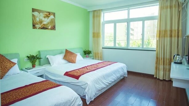 Een hotelkamer met twee bedden, een schilderij aan de muur, een raam met gordijnen en een nachtkastje met een plant.