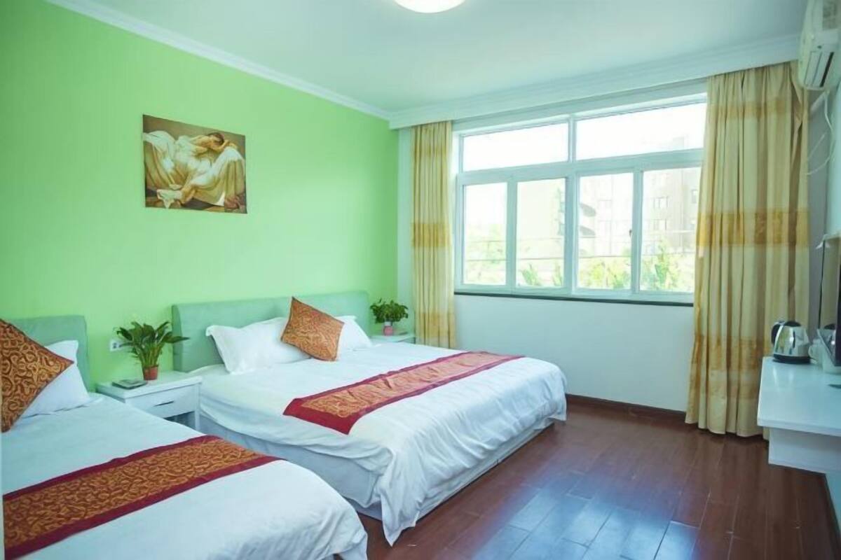 Habitación de hotel con dos camas, un cuadro en la pared, una ventana con cortinas y una mesita de noche con una planta.