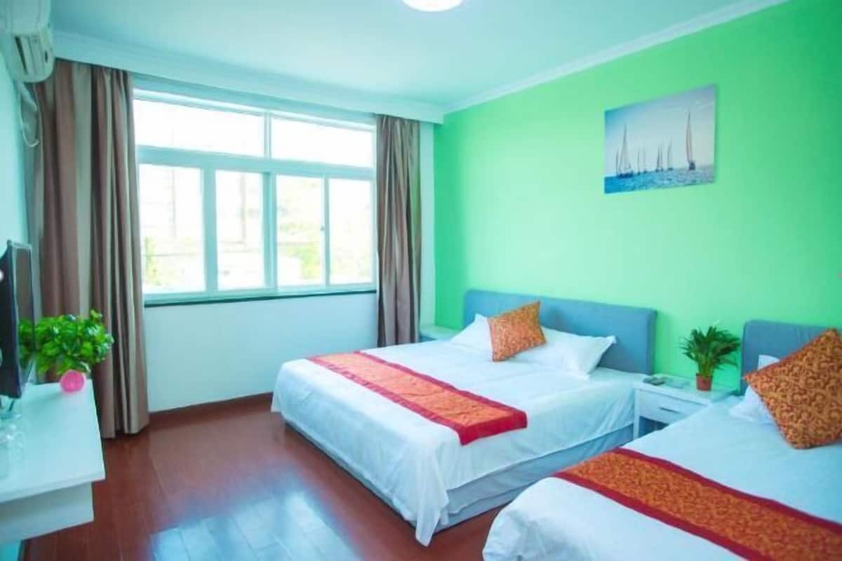 Une chambre d’hôtel avec deux lits, un bureau avec un ordinateur, une fenêtre avec des rideaux et un tableau au mur.