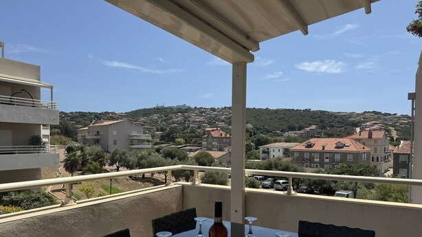 A balcony with a table, wine glasses, and a bottle, overlooking a residential area with buildings and trees. - QUATRINA L - Pretty T2 ideally located (PROPRIANO)