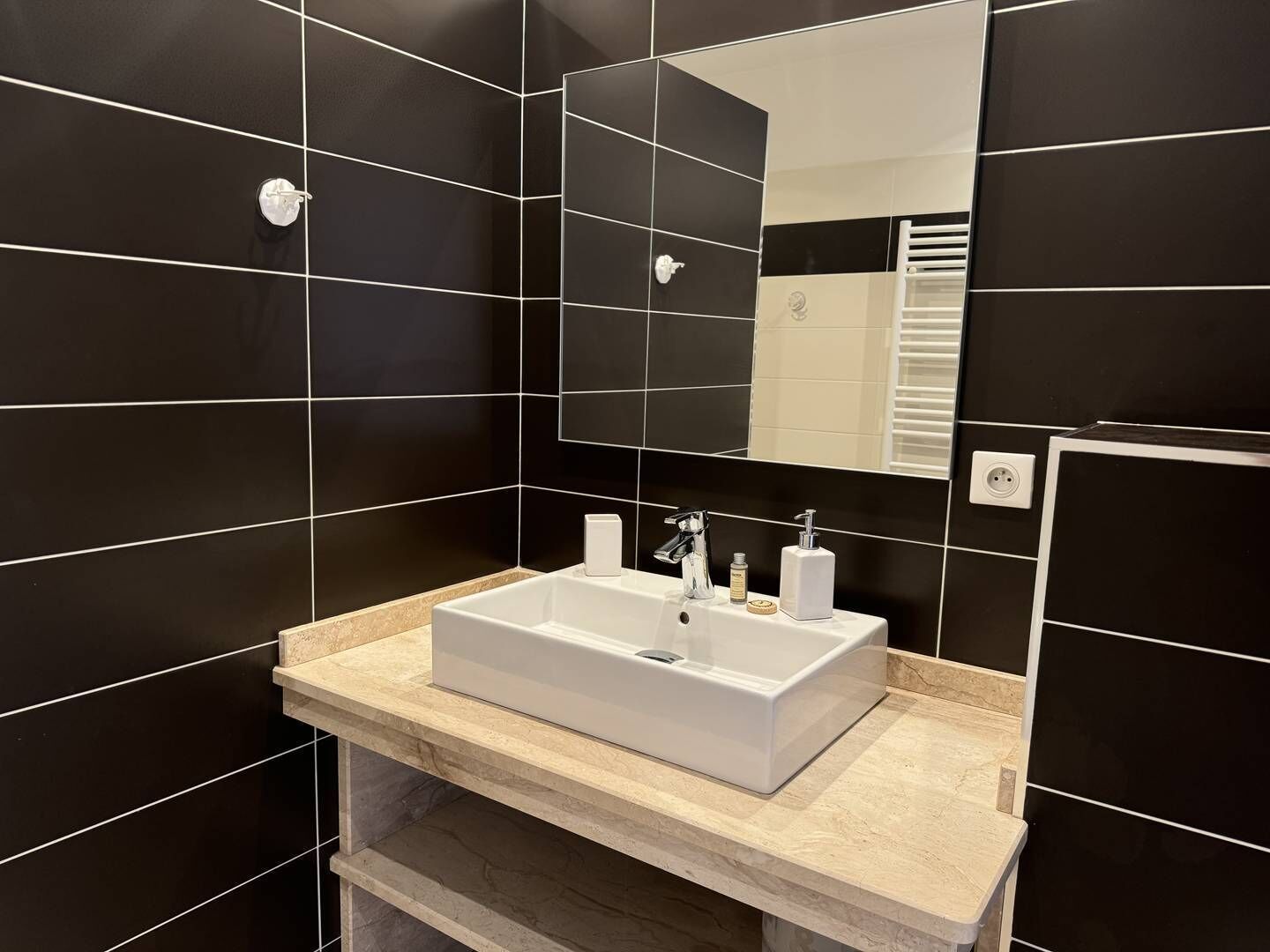 A modern bathroom with black tiled walls, a white sink, and a mirror.