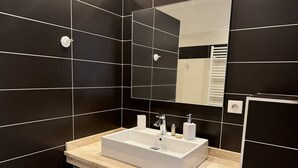 A modern bathroom with black tiled walls, a white sink, and a mirror. - QUATRINA L - Pretty T2 ideally located (PROPRIANO)