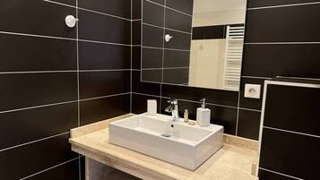A modern bathroom with black tiled walls, a white sink, and a mirror.
