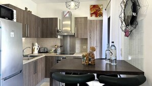 A modern kitchen with a central island, stainless steel appliances, and a geometric light fixture. - QUATRINA L - Pretty T2 ideally located (PROPRIANO)