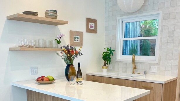 A modern kitchen with a white marble countertop, wooden stools, a small island, and a window with a view of greenery. - Casa Flora, Brand-New Serene Guest House in Los Angeles with WiFi, AC (Los Angeles)