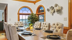 Une salle à manger avec une table en bois dressée pour six personnes, des chaises rembourrées et une grande fenêtre offrant une belle vue.