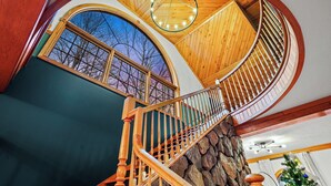 Un escalier en colimaçon avec des rampes en bois et une base en pierre, menant à un plafond élevé avec un revêtement en bois et une lucarne circulaire.