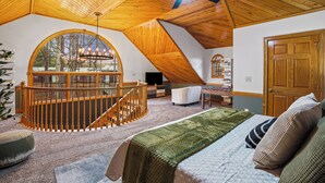 Une chambre avec une grande fenêtre, un plafond en bois et un lit recouvert d’une couverture verte.