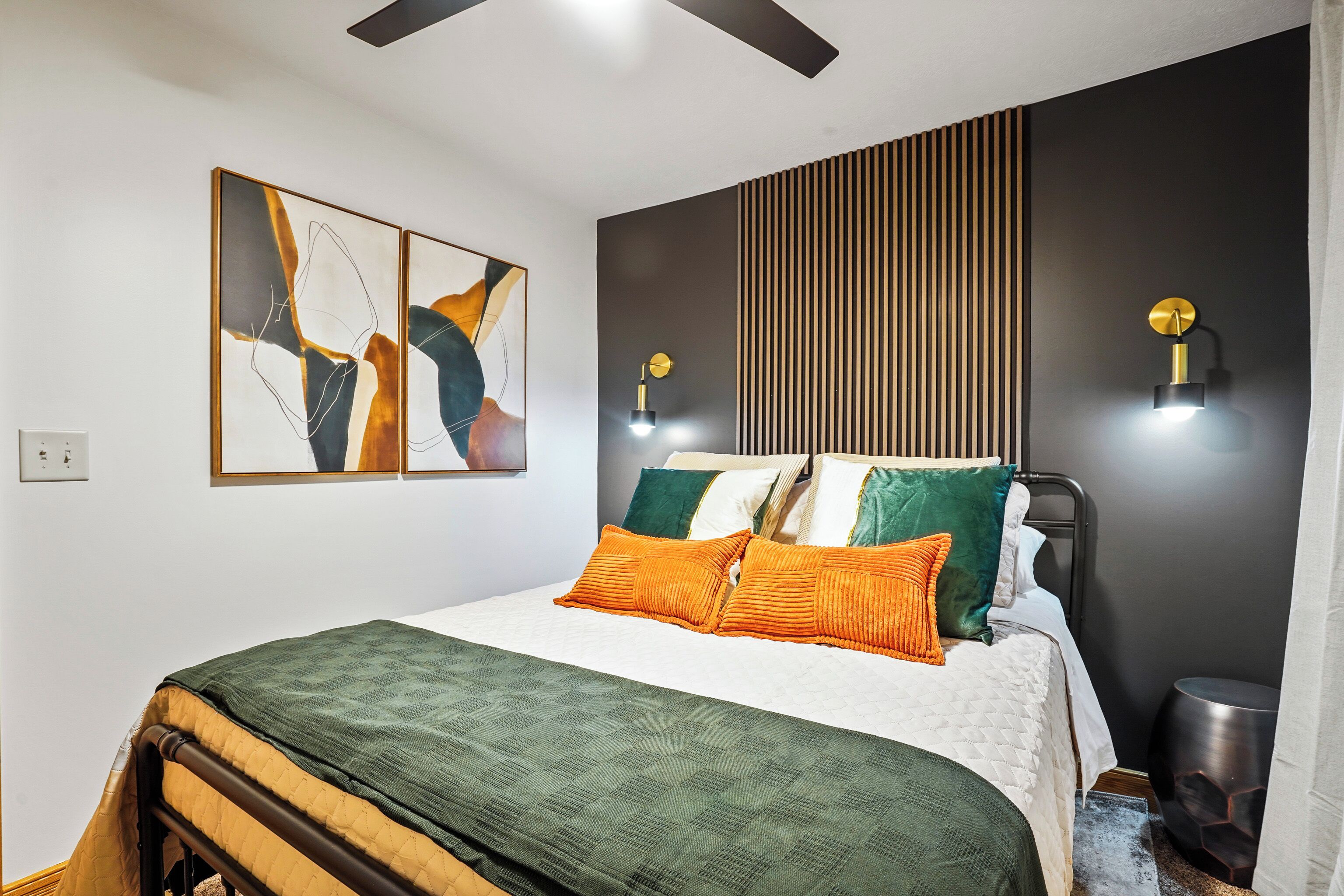 Une chambre à coucher moderne avec un lit, deux lampes fixées au mur et des œuvres d’art abstraites.