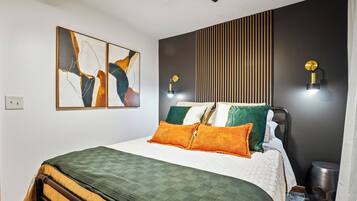 Une chambre à coucher moderne avec un lit, deux lampes fixées au mur et des œuvres d’art abstraites.