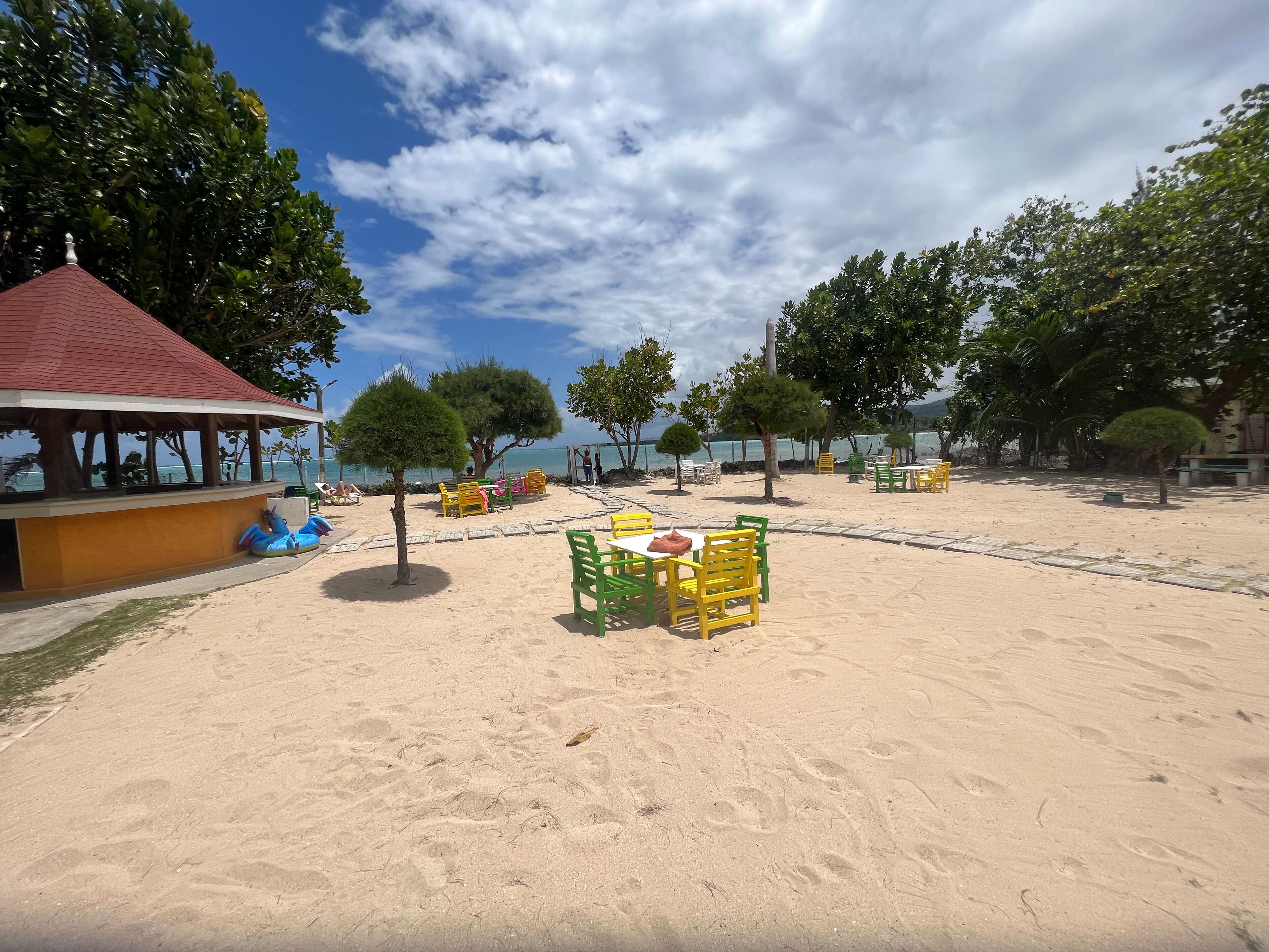 Zona de playa con pabellón, asientos y árboles.