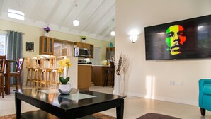 A modern living room with a black coffee table, a sofa, and a teal armchair. There is a kitchen in the background with wooden cabinets and a microwave. - Avant Family Villa (St. Ann's Bay)