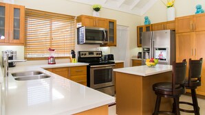 A modern kitchen with wooden cabinets, stainless steel appliances, a large island with bar stools, and decorative vases. - Avant Family Villa (St. Ann's Bay)