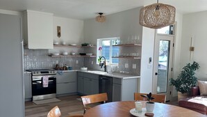 Une cuisine moderne avec des armoires blanches, un four encastré et un coin repas comprenant une table et des chaises en bois.