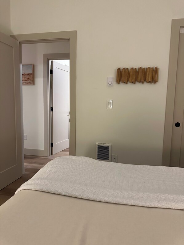 A bedroom with a bed, a radiator, a wall-mounted light switch, and a door leading to another room. - Newly built, 2-bedroom loft, high desert sunsets & mountain peaks, A/C and Wifi (Redmond)