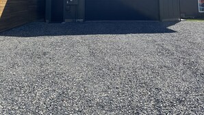 Un bâtiment à deux étages avec un garage, une clôture en bois et une allée gravillonnée.