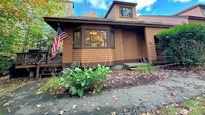 A two-story house with a brick exterior, a chimney, and a porch with a wooden railing. - F26 Bretton Woods home steps from the slopes, AC, pool passes, discounted cog tix! (Bretton Woods)