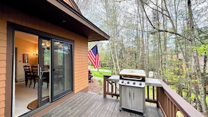 A wooden deck with a grill and an American flag, overlooking a forested area. - F26 Bretton Woods home steps from the slopes, AC, pool passes, discounted cog tix! (Bretton Woods)