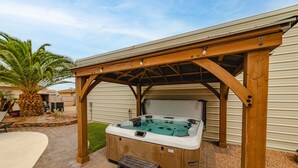 Ein Whirlpool unter einer Holzpergola mit einer Ziegelterrasse und einer Palme im Hintergrund.