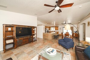 A spacious living room with a large flat-screen TV, a ceiling fan, and a kitchen area in the background. - Sparkling Pool/Spa/Game Room/ RV Port (Lake Havasu City)