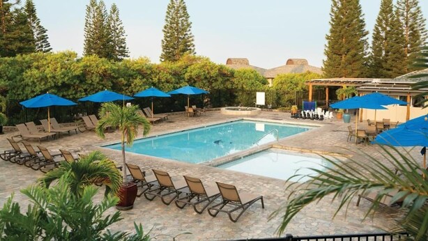 A pool area with lounge chairs and umbrellas, surrounded by trees and a building.