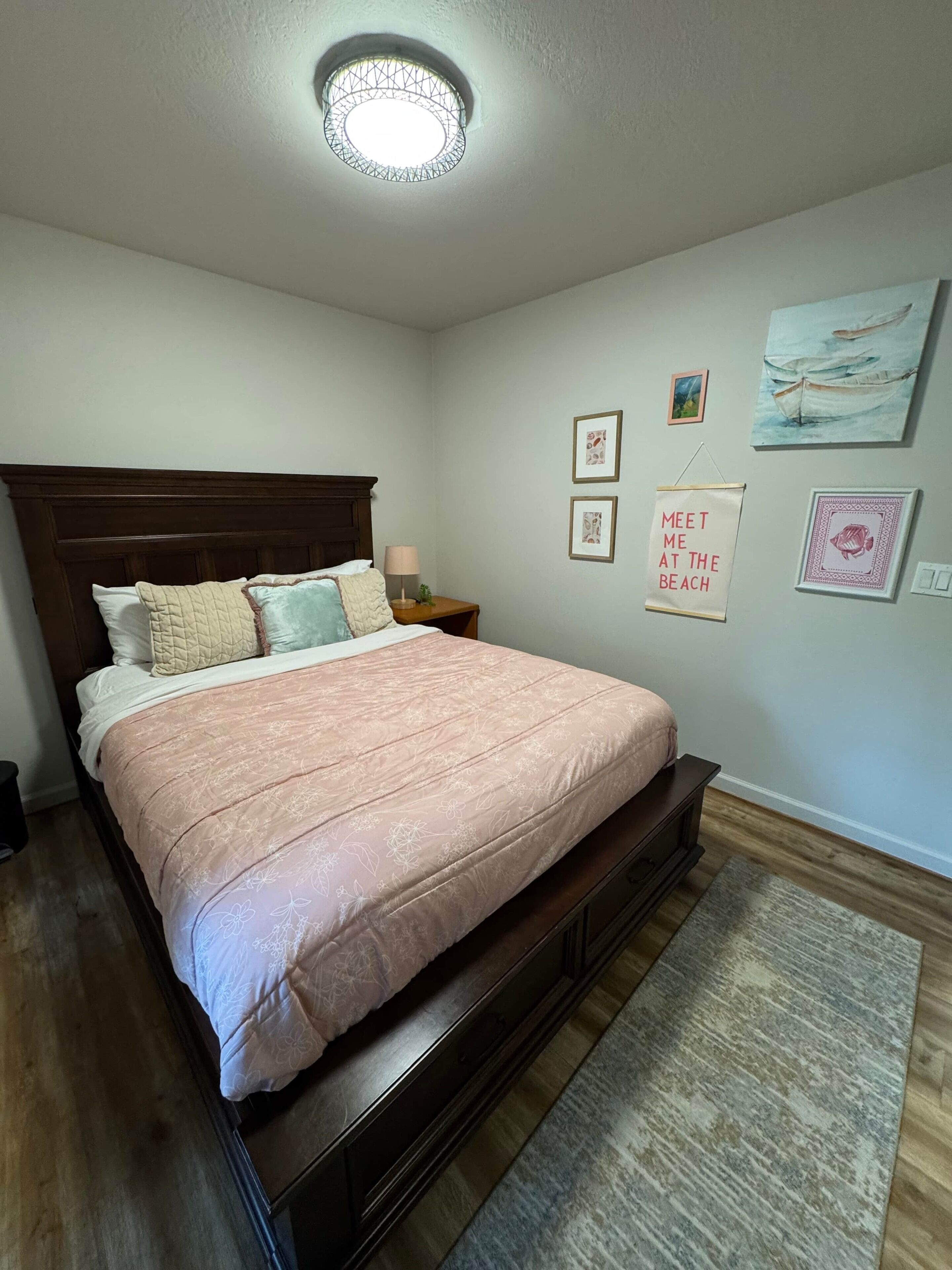 A bedroom with a wooden bed, a nightstand, a wall-mounted lamp, and framed artwork.