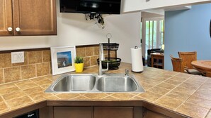 A kitchen with a double sink, wooden cabinets, a mounted TV, and a wall-mounted wooden turtle decoration.