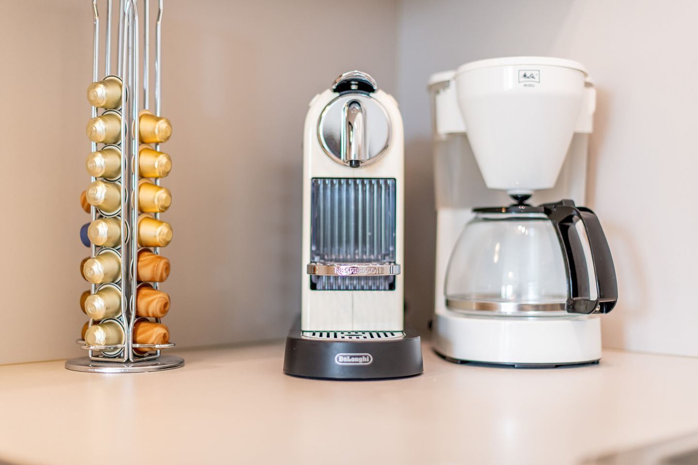 Un plan de travail de cuisine avec une machine à café, un cuiseur à riz et un récipient vertical doté de plusieurs compartiments.