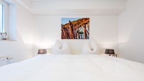 A large bed with white bedding, two bedside tables with lamps, and a painting on the wall. - Raantem Hüs Whg. 1 - Wattblick. Naturnah. Terrasse (Rantum)