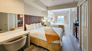 A hotel room with a large bed, a desk, and a chair. There is a kitchenette area with cabinets and a microwave.