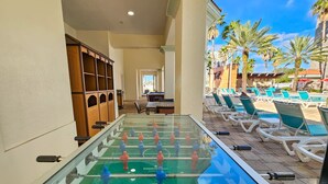 A foosball table in a corridor with lounge chairs and palm trees in the background.