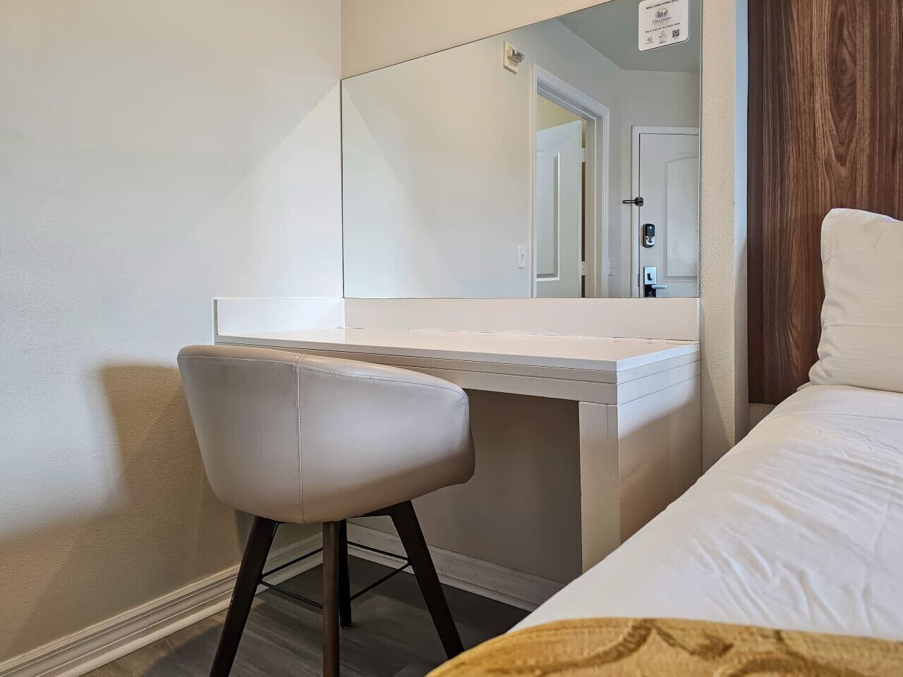Ett hotellrum med en säng, ett vitt skrivbord, en stol och en stor spegel.