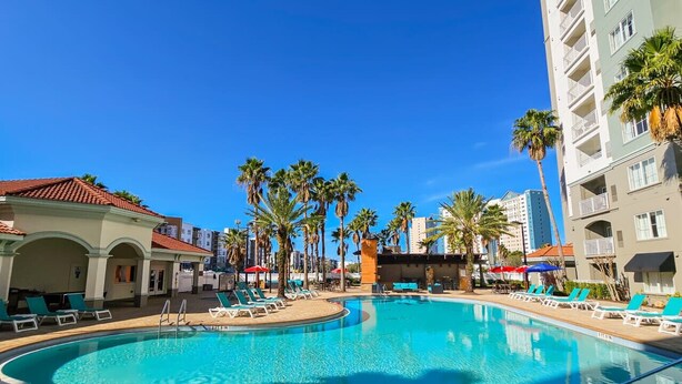 A resort pool area with lounge chairs, palm trees, and a clear blue sky.