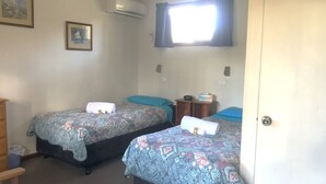 A room with two beds, each with patterned bedding and towels, a small wooden nightstand, a window with curtains, and an air conditioning unit on the wall. - Cabin 5 - 2 single beds and ensuite. Access to all amenities (O'Connell)