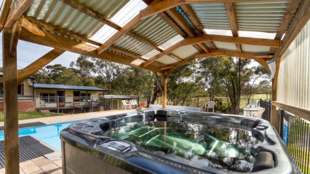 A hot tub under a wooden pergola with a pool in the background. - Cabin 5 - 2 single beds and ensuite. Access to all amenities (O'Connell)