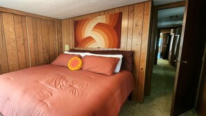 Ein Zimmer mit einer holzgetäfelten Wand, einem Bett mit einem pfirsichfarbenen Bettbezug und einem großen abstrakten Gemälde darüber.