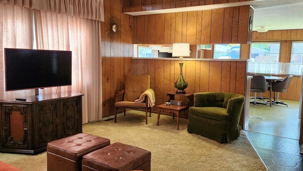 Ein gemütliches Wohnzimmer mit Flachbildfernseher, einem grünen Sessel, einem braunen Sessel und einem Holzschrank.