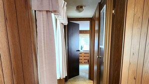 Ein Flur mit Holzwänden und Teppichboden, der zu einem Zimmer mit Fenster und Tür führt.