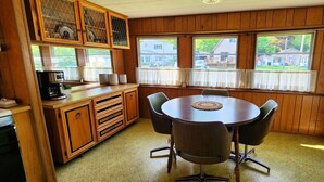 Ein Zimmer mit Holzwänden, einem runden Tisch mit Stühlen, einer Kaffeemaschine und einem Fenster mit Vorhängen.