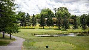 Un campo de golf con un estanque, árboles y un edificio al fondo.