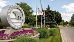 Señal del Grand Traverse Resort and Spa con un logotipo de oso, rodeada de flores y banderas.