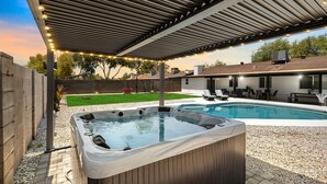 Um quintal com hidromassagem, piscina e área de varanda coberta.