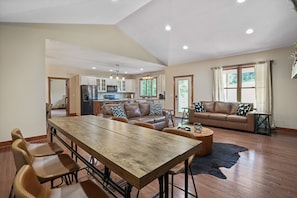 Amplia sala de estar con una mesa de comedor de madera, sofás de cuero y una cocina al fondo.