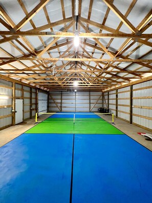 Un gimnasio con techo alto y vigas de madera, con piso azul y verde.
