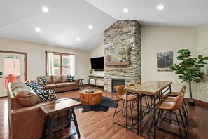 A spacious living room with a stone fireplace, leather sofas, a wooden coffee table, and a dining area with bar stools.