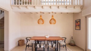 Een eethoek met een houten tafel, zes stoelen, twee hanglampen, een witte mand en een lijst met een afbeelding aan de muur.