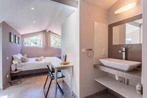 A bedroom with a bed, bedside table, and a desk with a chair. The bathroom has a sink, mirror, and towel rack. - Villa Atolla - Welkeys (Capbreton)