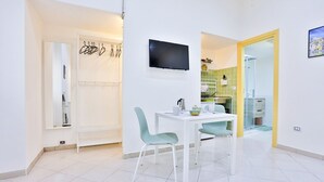 A modern kitchen with a TV, white cabinets, and a dining area with two chairs. - GuestHost - Track Station Studio Apartment - with Netflix (Napoli)