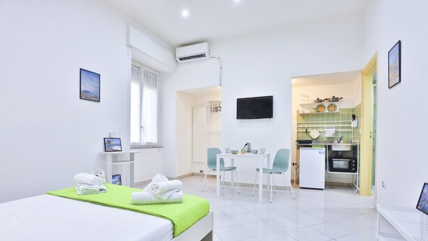 A hotel room with a bed, a desk, a chair, a small kitchenette, and a TV. - GuestHost - Track Station Studio Apartment - with Netflix (Napoli)