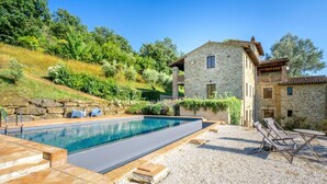 Una casa in pietra con piscina, area relax all'aperto e giardino in pendenza.
